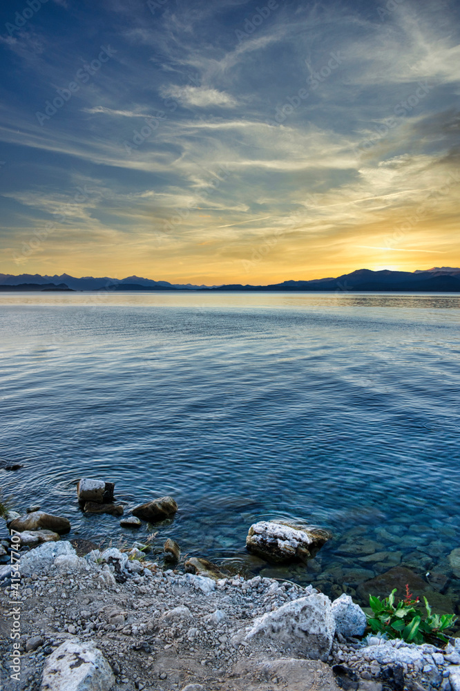 stony shoreline over a lake at sunset with mountains in the background