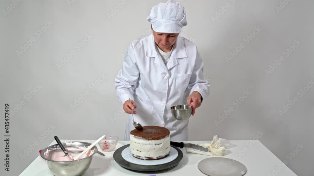 A middle-aged woman baker pours syrup on a wedding cake with chocolate brownies. A middle-aged woman baker pours syrup on a wedding cake with chocolate brownies.
