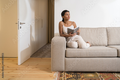 Woman reading book while looking in distance and dreaming