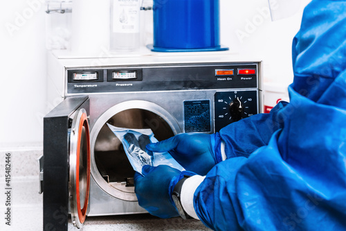 unrecognizable person in bio security suit holding tools and putting them into a machine to sterilize them.