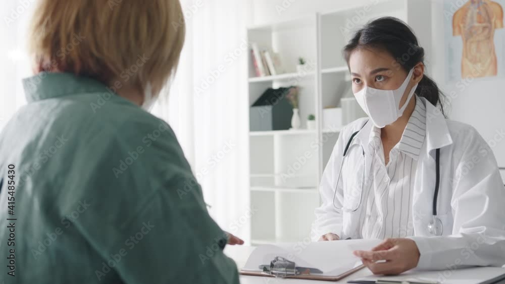 Young Asia lady doctor wear protective mask using clipboard is delivering great news talk discuss results or symptoms with girl patient in hospital office. Lifestyle new normal after corona virus. Young Asia lady doctor wear protective mask using clipboard is delivering great news talk discuss results or symptoms with girl patient in hospital office. Lifestyle new normal after corona virus.