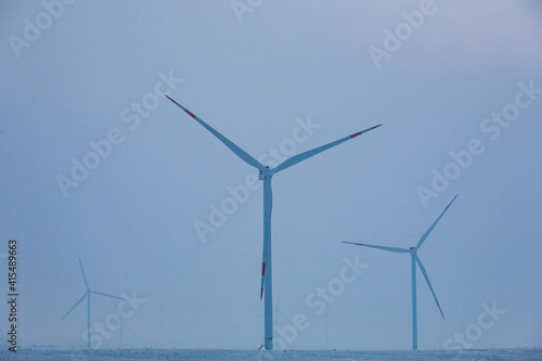 Field of wind turbine towers with large blades in winter on background of snow at sunrise