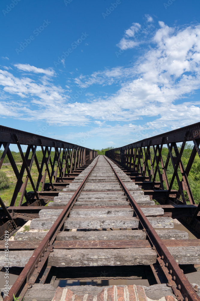 Abandoned iron railway bridge over a stream with a sky and clouds background