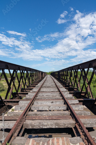 Abandoned iron railway bridge over a stream with a sky and clouds background © Carlos G. Baquero