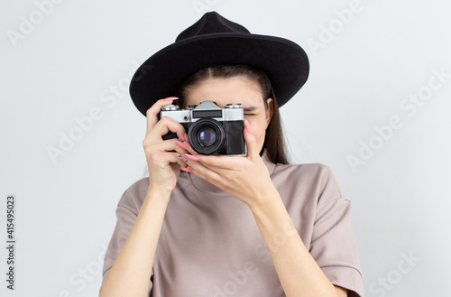 European woman holding retro photocamera and taking a photo over white background in studio