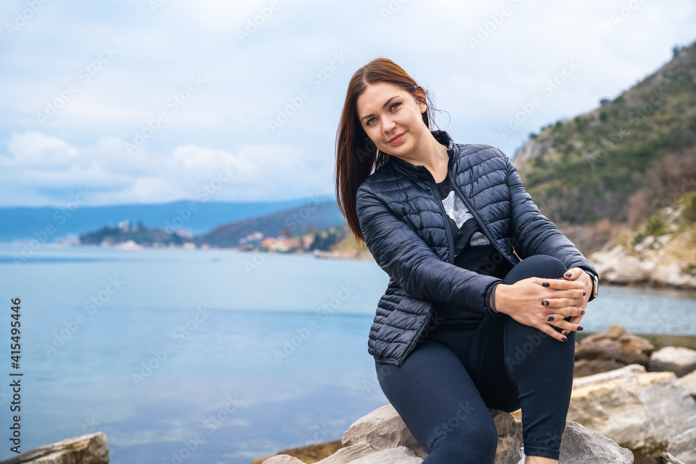 Smiling young attractive woman posing outdoor against mountains and and blue lake or sea.