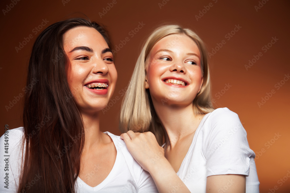 two pretty diverse girls happy posing together: blond and brunette, caucasian and asian on brown background, lifestyle people concept two pretty diverse girls happy posing together: blond and brunette, caucasian and asian on brown background, lifestyle people concept
