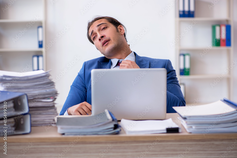 Young male employee unhappy with excessive work in the office Young male employee unhappy with excessive work in the office
