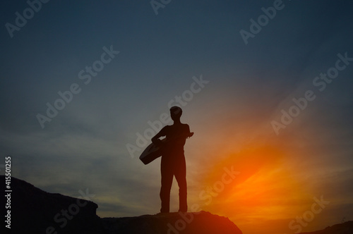 The silhouette of a man holding a guitar on a high hill