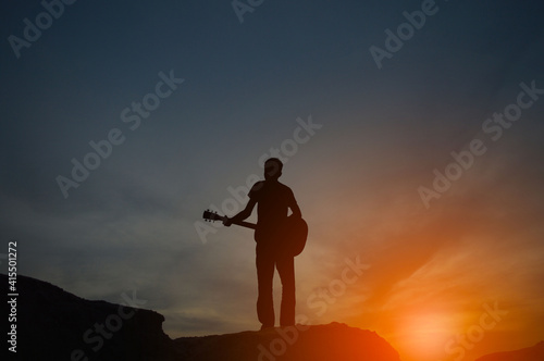 The silhouette of a man holding a guitar on a high hill