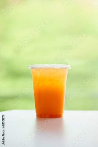 DISPOSABLE PLASTIC CUP DRINKS , plastic cup of tea for takeaway place on white table on green background. Close up and selective focus