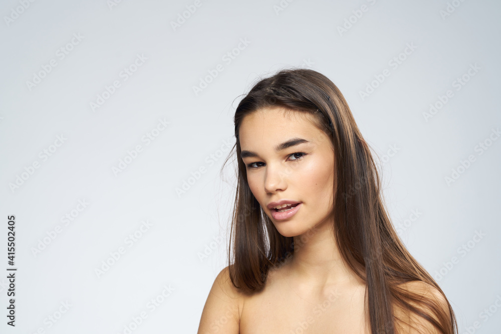 Pretty brunette naked shoulders long hair close-up light background Pretty brunette naked shoulders long hair close-up light background