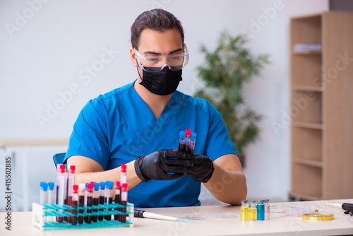 Young male biochemist testing blood samples in pandemic concept