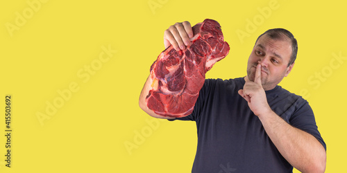 fat man holds a raw piece of meat in his hand. person cannot eat meat he is on a diet or a vegetarian. celebrating International Day Without Meat and World Vegetarian Day. support for vegetarianism.