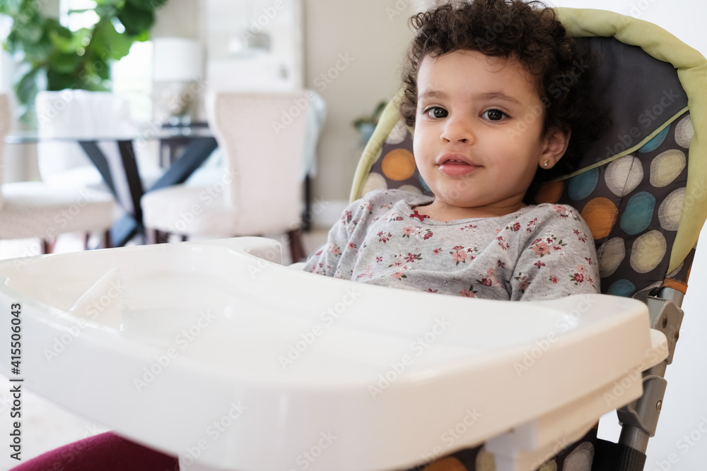 Cute two year old baby girl sitting on a high chair in a home setting Cute two year old baby girl sitting on a high chair in a home setting