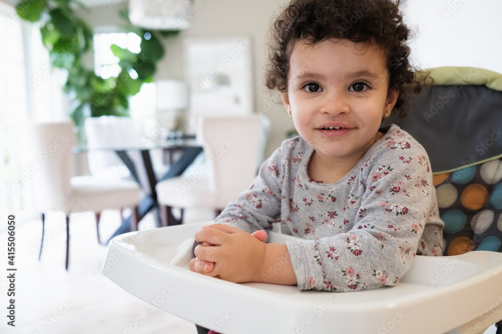 Cute two year old baby girl sitting on a high chair in a home setting Cute two year old baby girl sitting on a high chair in a home setting
