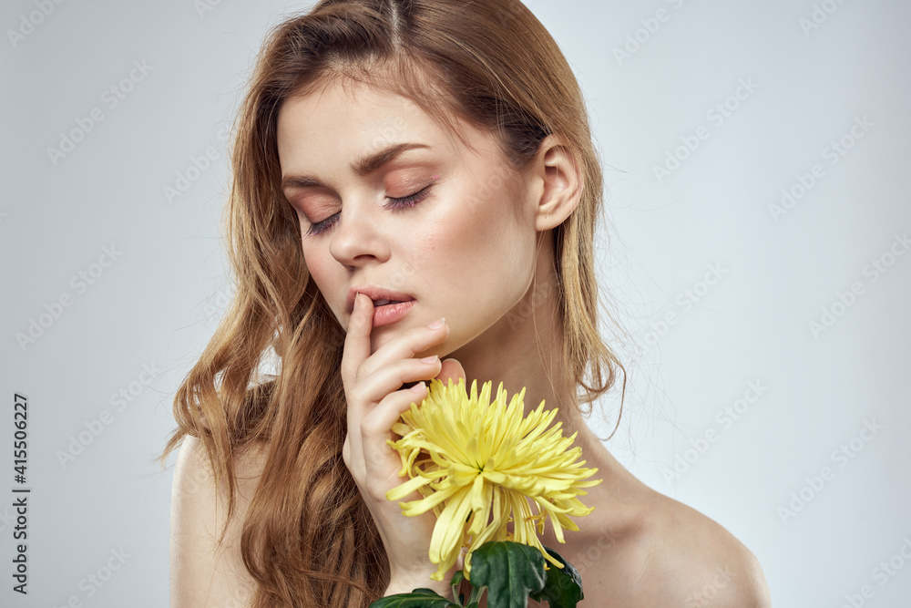 Portrait of a beautiful woman with a yellow flower on a light background charming smile model red hair Portrait of a beautiful woman with a yellow flower on a light background charming smile model red hair