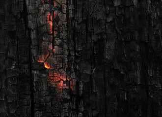 Dark black background of burnt wood with red hot embers still burning.