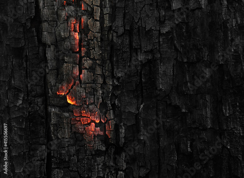 Dark black background of burnt wood with red hot embers still burning.