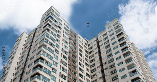 Tall city buildings and a plane flying overhead in the sky.Concept of doing something different from others for business purpose .