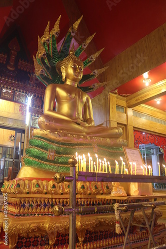 Golden Buddha statue Do meditation Behind there is a 9-headed green Naga, in the front there is a candle lit to brighten. Sacred things that Buddhists worship. Photo at temple in Thailand