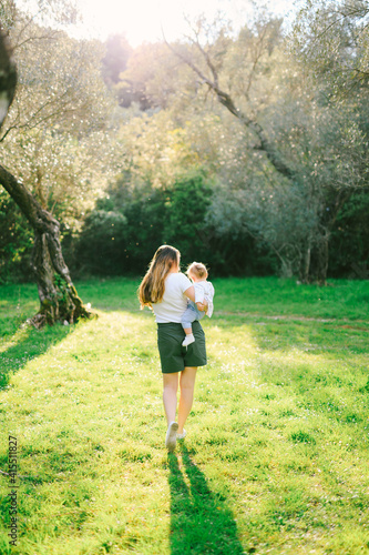 Woman walking under an olive tree with her daughter in her arms