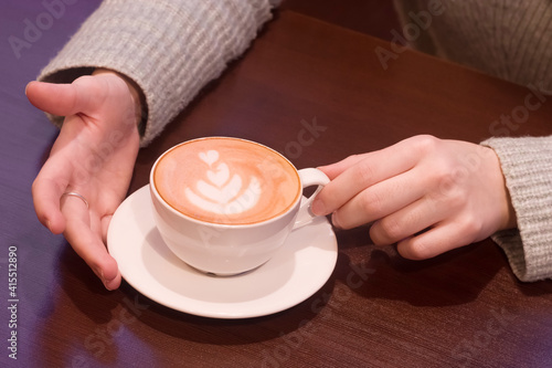 Empty space for logo. A cup of cappuccino in a hands of a woman.