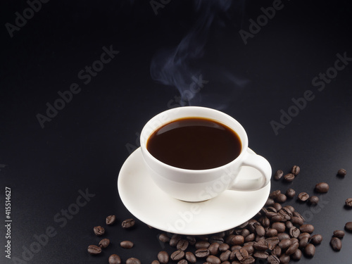 A cup of hot black coffee on black background with with roasted coffee beans and hot steam