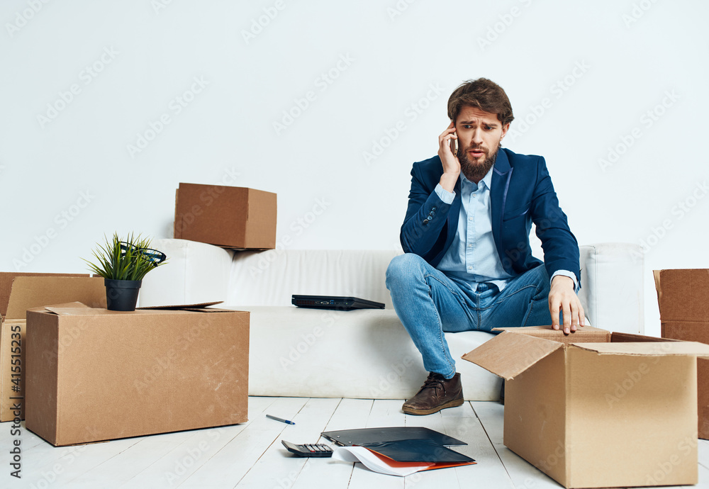 Business man with laptop sitting on sofa unpacking boxes official Business man with laptop sitting on sofa unpacking boxes official