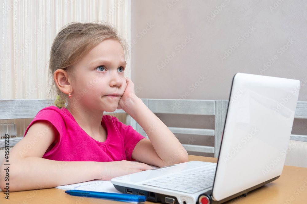 Cute little girl student sits at the table and thinks how to do homework. A girl is watching a video tutorial on a laptop. Learning concept, distance learning, video conferencing lesson with mentor Cute little girl student sits at the table and thinks how to do homework. A girl is watching a video tutorial on a laptop. Learning concept, distance learning, video conferencing lesson with mentor