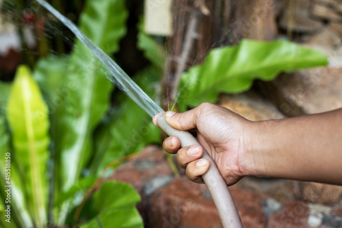 asian dark skinned female hand with garden hose watering plants. close up, soft focus
