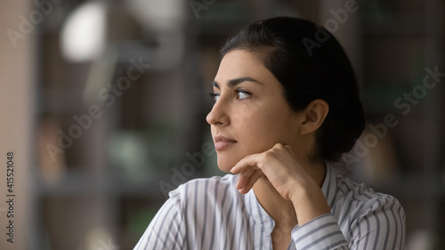 Close up of pensive Indian woman look in distance thinking pondering or life choices make solution. Thoughtful millennial mixed race ethnicity female decide or plan. Visualization concept.