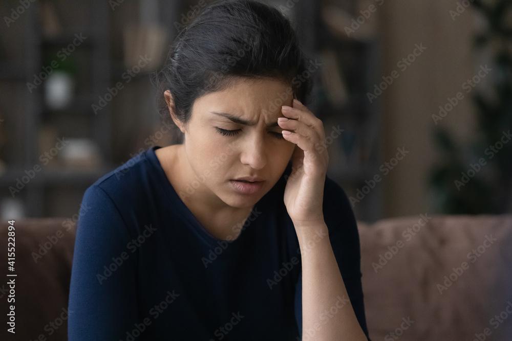 Ill millennial Indian woman suffer from migraine or headache at home. Unhealthy sick young mixed race female struggle with dizziness or blurry vision, infected with covid-19. Health problem concept. Ill millennial Indian woman suffer from migraine or headache at home. Unhealthy sick young mixed race female struggle with dizziness or blurry vision, infected with covid-19. Health problem concept.