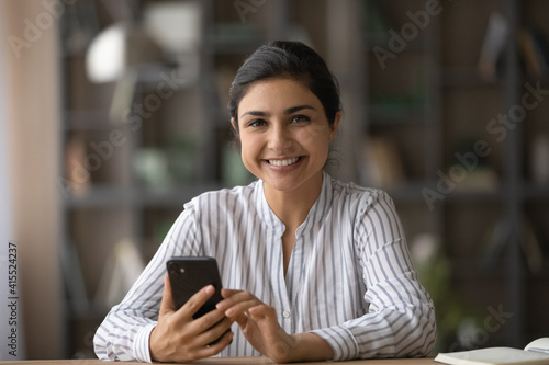 Portrait of smiling young Indian woman client or user hold modern smartphone gadget shopping online. Happy millennial mixed race female use cellphone texting messaging on web. Technology concept.
