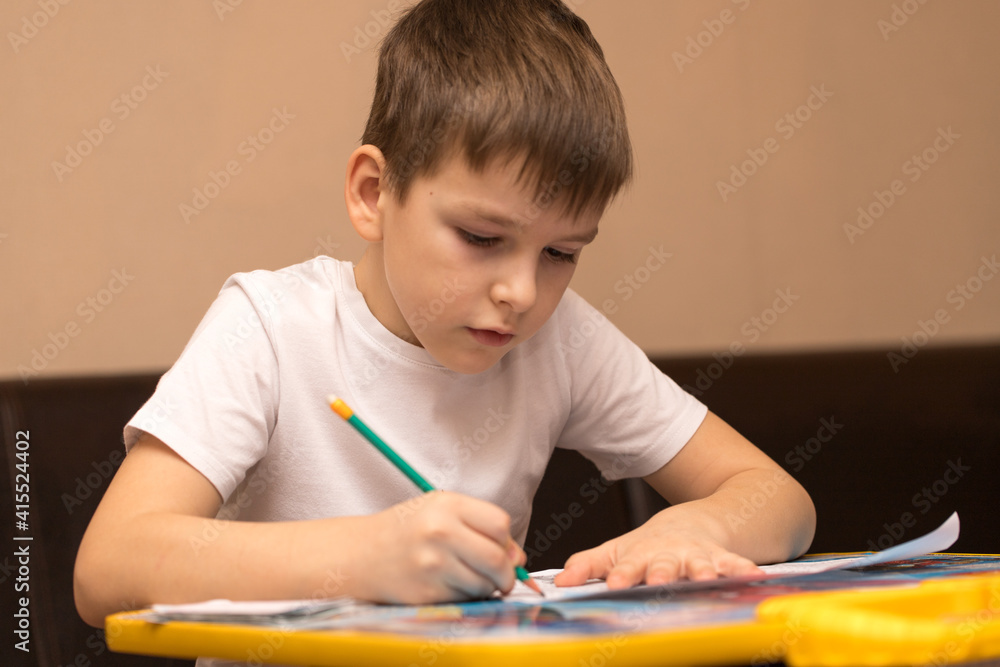 boy of six years writes with a pencil sitting at the table. close-up boy of six years writes with a pencil sitting at the table. close-up