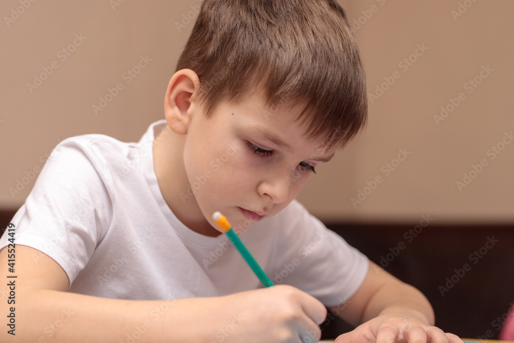boy of six years writes with a pencil sitting at the table. close-up boy of six years writes with a pencil sitting at the table. close-up