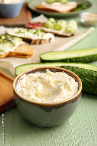 Bowl with tasty cream cheese on color wooden background