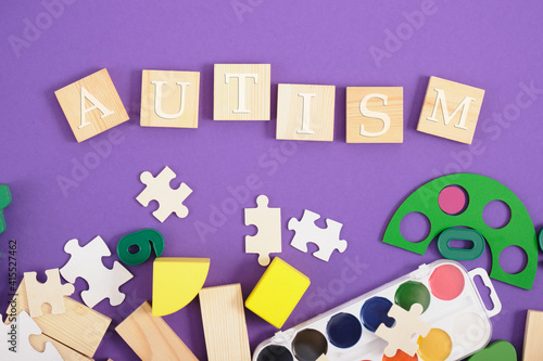 inscription autism on wooden squares, purple background, copy space, developmental toys and paints for training and diagnosis