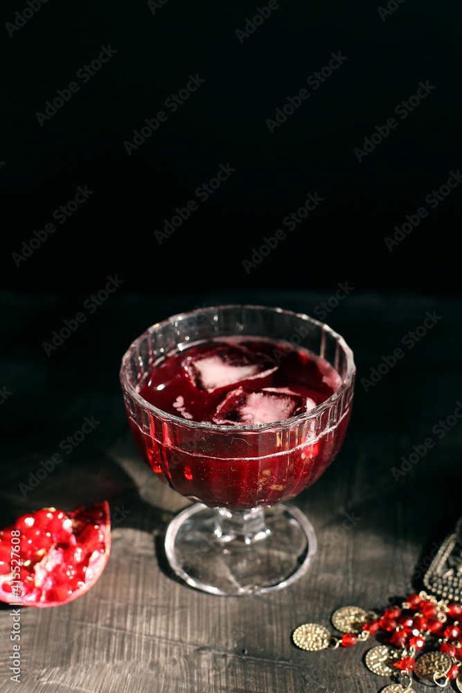 Ruby red pomegranate juice in a glass with ice on a rustic dark mystical background Ruby red pomegranate juice in a glass with ice on a rustic dark mystical background