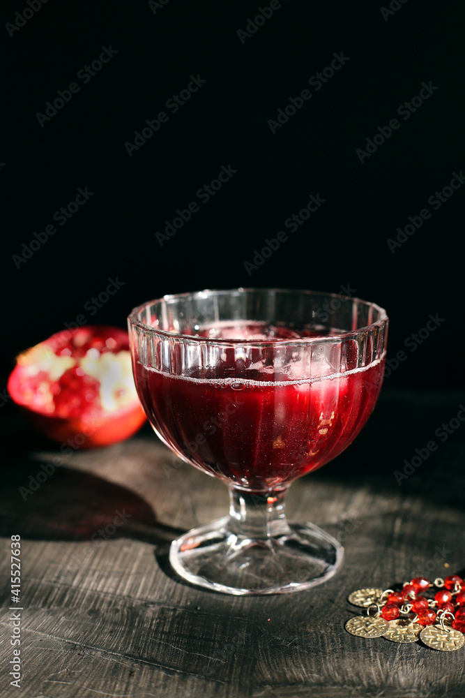 Ruby red pomegranate juice in a glass with ice on a rustic dark mystical background Ruby red pomegranate juice in a glass with ice on a rustic dark mystical background