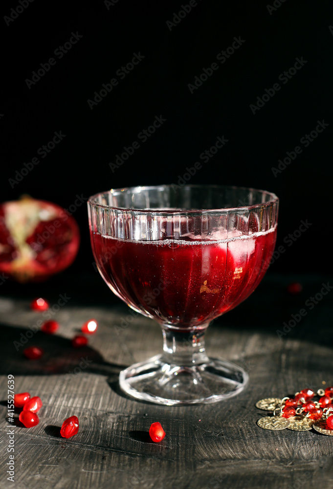Ruby red pomegranate juice in a glass with ice on a rustic dark mystical background Ruby red pomegranate juice in a glass with ice on a rustic dark mystical background