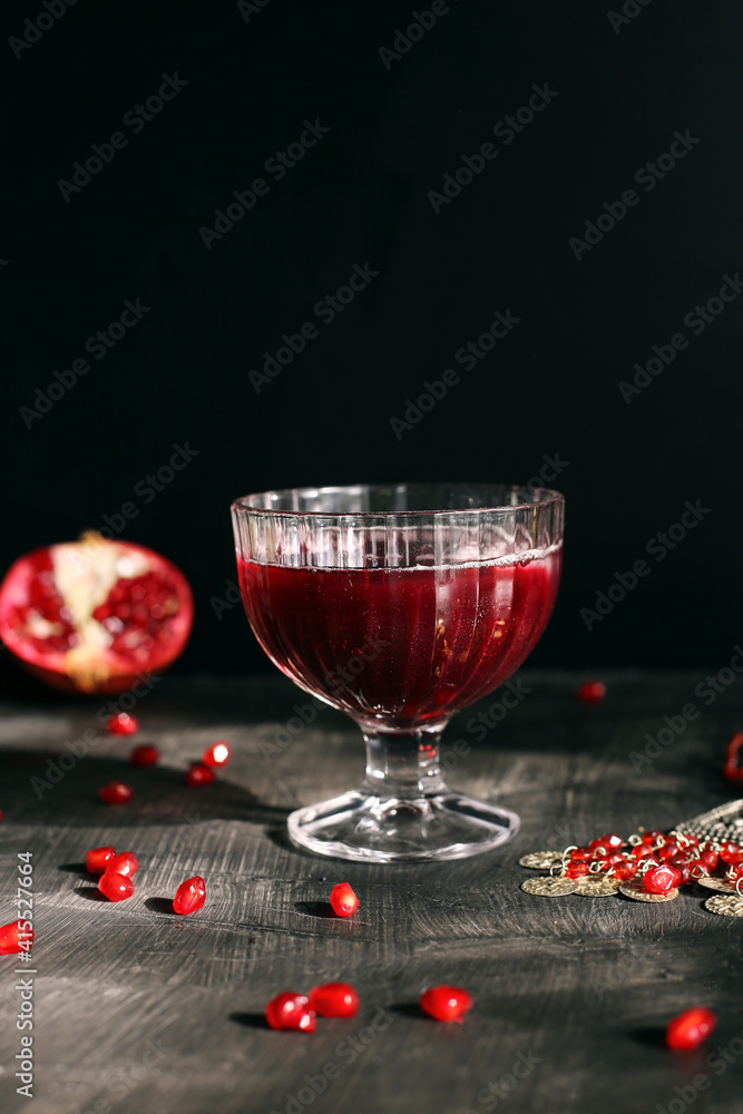 Ruby red pomegranate juice in a glass with ice on a rustic dark mystical background Ruby red pomegranate juice in a glass with ice on a rustic dark mystical background