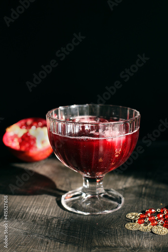 Ruby red pomegranate juice in a glass with ice on a rustic dark mystical background