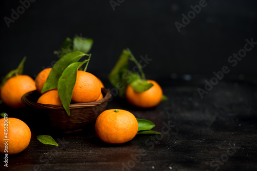 Dark mood fresh orange clementines with green leaves in a basket on a dark table