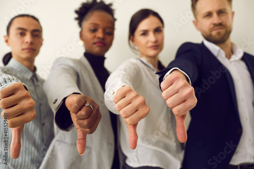 Group of young diverse people giving thumbs down, hands in closeup. Multiracial corporate HR managers saying no and refusing a person. Multiethnic business team showing dislike of bad work photo