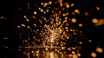 spark in a dark background from a hot red metal cut by a steel cutting machine in a factory. Nice bokeh in warm black background. Flashes from cutting iron