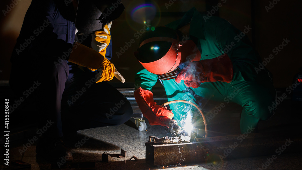 mechanics workers work overtime hardly at night in a factory. Engineers wearing safety outfits with mechanic jumpsuits, gloves, boots, and welding helmets working on metal welding mechanics workers work overtime hardly at night in a factory. Engineers wearing safety outfits with mechanic jumpsuits, gloves, boots, and welding helmets working on metal welding