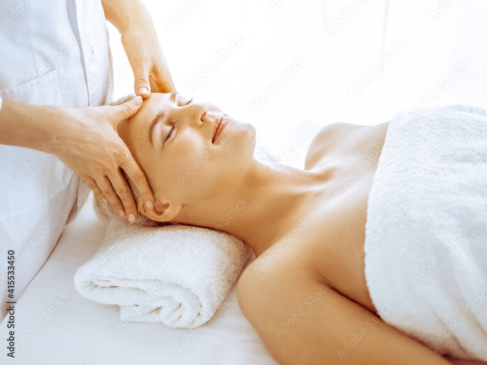 Beautiful blonde woman enjoying facial massage in spa center. Relaxing treatment in medicine and beauty concepts Beautiful blonde woman enjoying facial massage in spa center. Relaxing treatment in medicine and beauty concepts