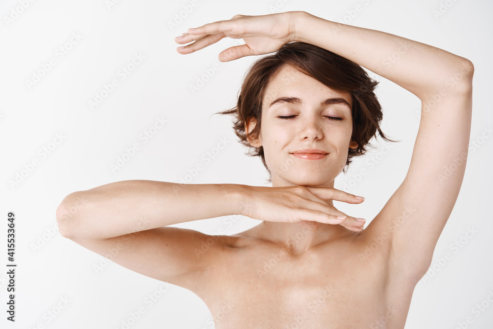 Obraz premium Smiling caucasian girl showing glowing healthy facial skin, standing half naked on white background. Young woman with hydrated and nourished face looking happy