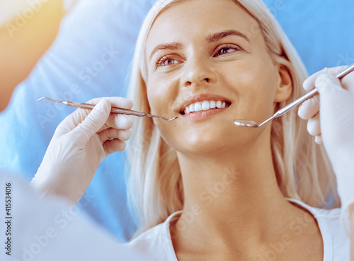 Smiling blonde woman examined by dentist at dental clinic. Healthy teeth in medicine concept